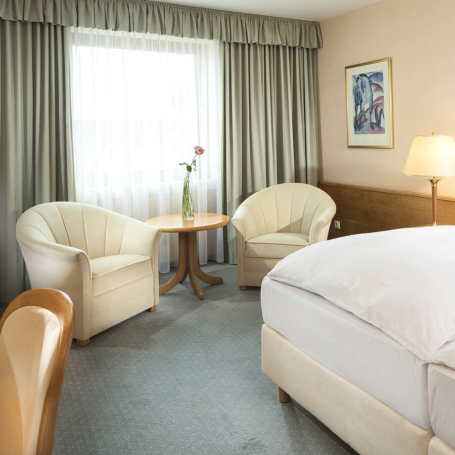 Chambre d’hôtel lumineuse avec deux lits, coin salon et grande fenêtre au Maritim Hotel Magdeburg