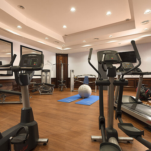 Salle de fitness moderne avec appareils de cardio, haltères et tapis de yoga à l’hôtel Maritim Ulm.