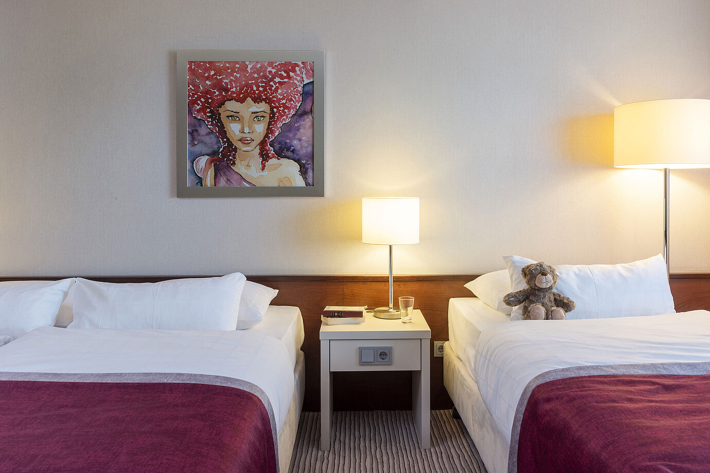Habitación familiar clásica en el Hotel Maritim Bonn con dos camas, mesa de noche y arte moderno para una estancia cómoda.