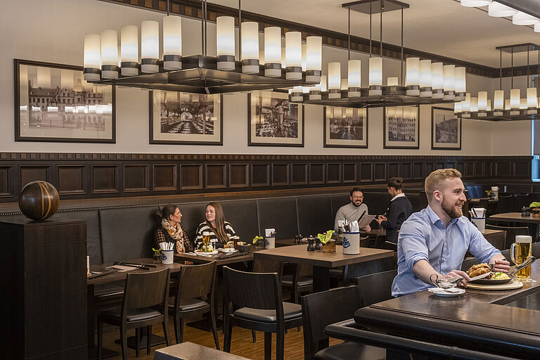 Clientes disfrutando de comidas en el acogedor restaurante "Rheinische Stov" del Maritim Düsseldorf con interior elegante.