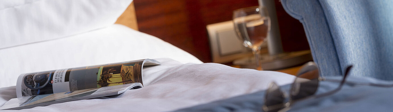  Close-up of a hotel room at Maritim Hotel Fulda with bed, magazine, glasses, and a glass of water on the nightstand.