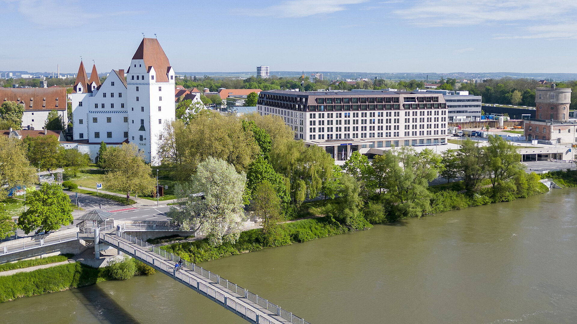 Aerial view of Maritim Hotel Ingolstadt overlooking the Danube, a pedestrian bridge, and the historic castle.