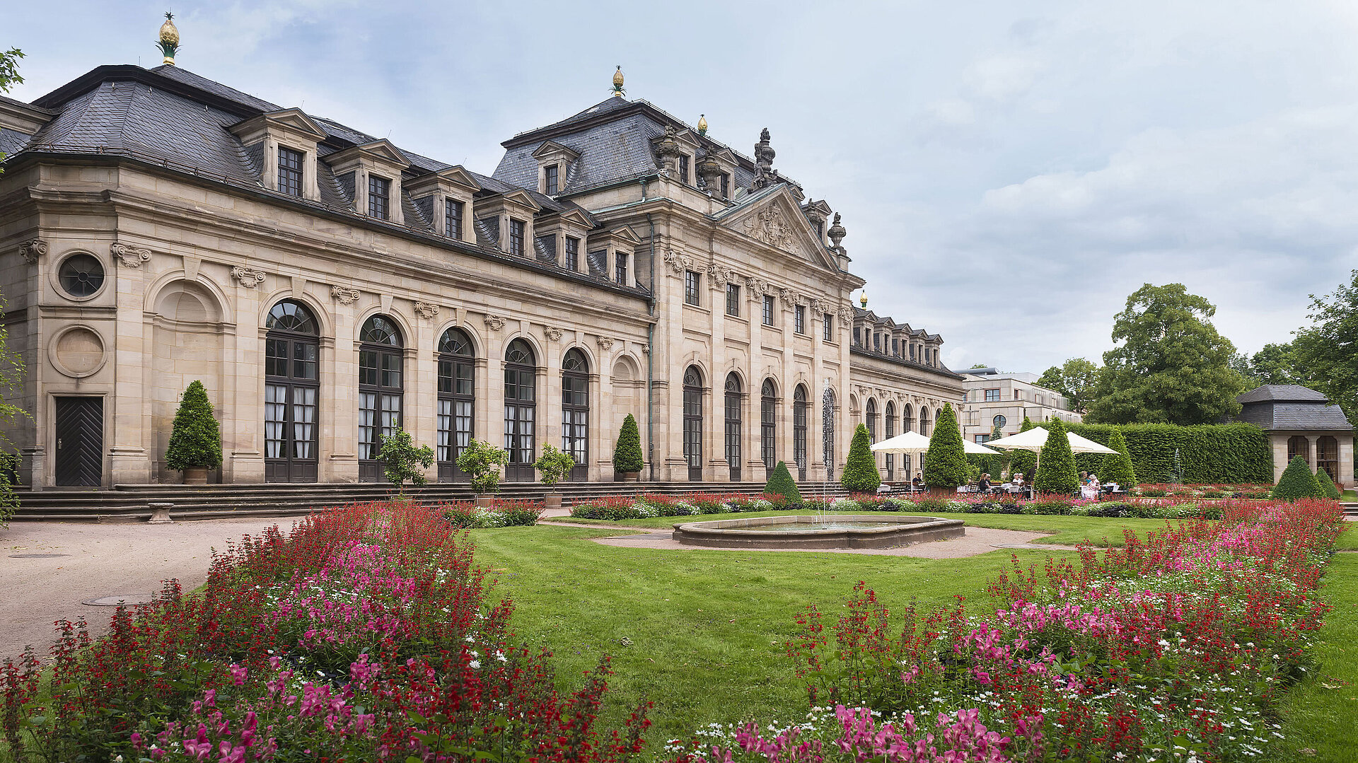 The historic Orangerie in Fulda with a baroque facade, staircase, and blooming garden in the foreground.
