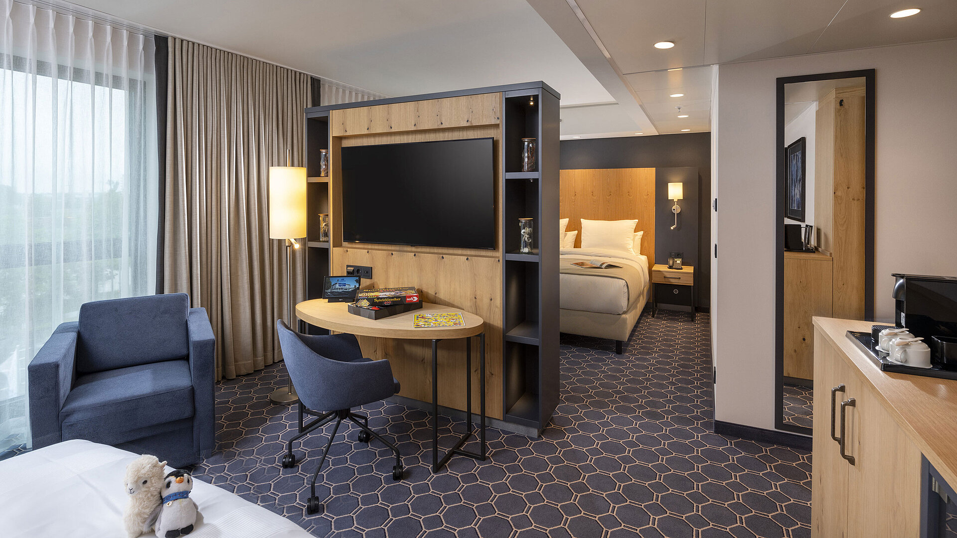 Bright room at Maritim Hotel Ingolstadt with seating area, desk, large TV, and view of the green surroundings.