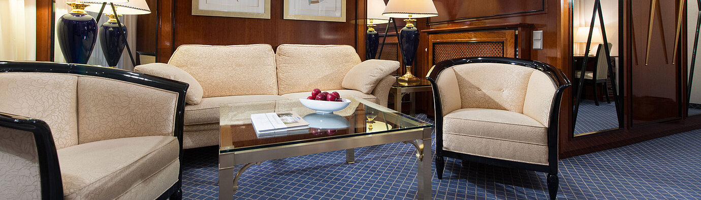 Elegant living area of a suite at Maritim Hotel Fulda with stylish furniture, glass coffee table, and cozy lighting.