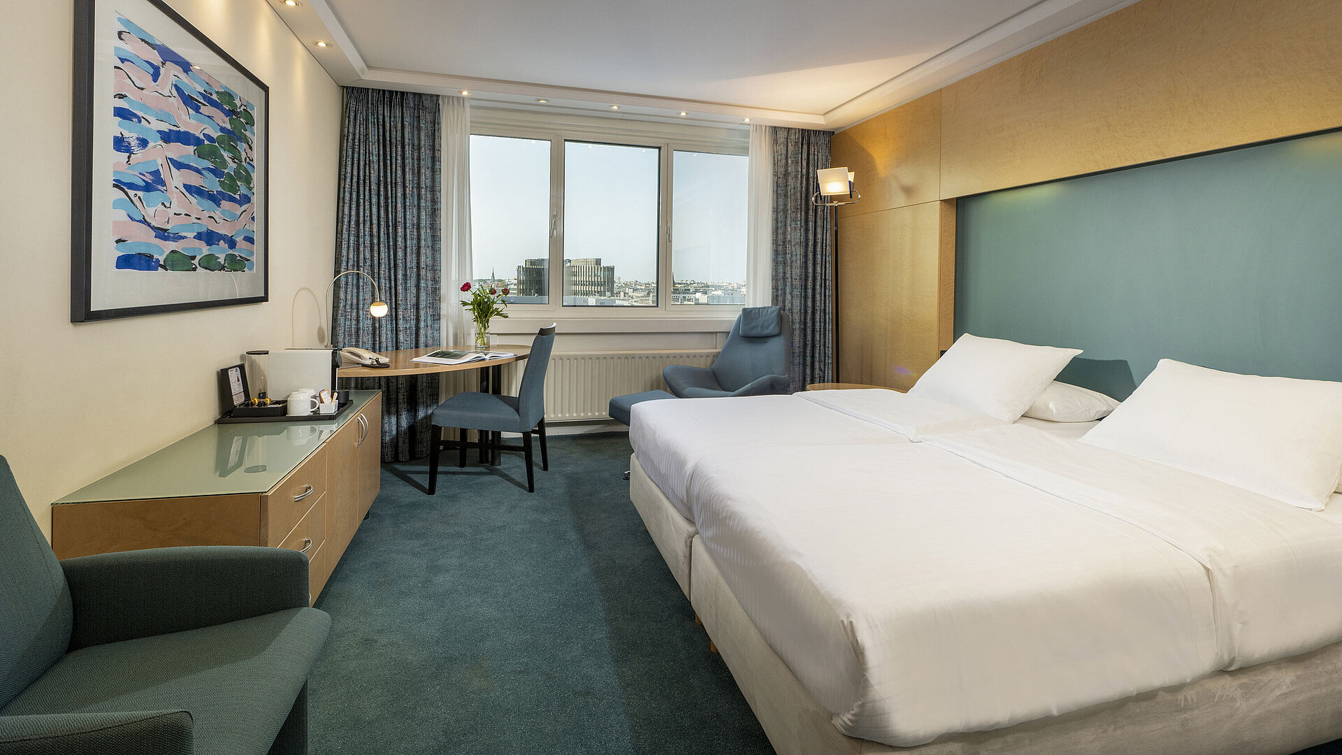 Camera Superior arredata in stile moderno presso l'hotel Maritim con letto grande,scrivania, opera d'arte e vista sulla città