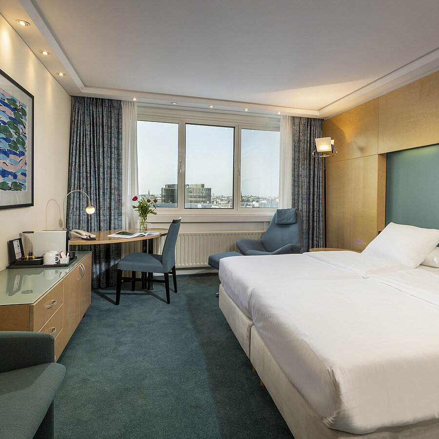 Habitación Superior modernamente amueblada en el hotel Maritim con cama grande, escritorio, obra de arte y vista a la ciudad.