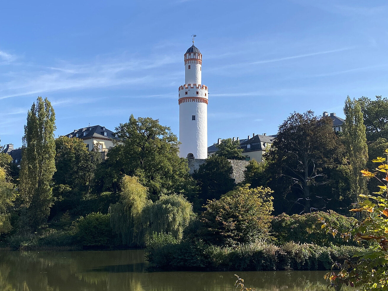 Torre blanca en Bad Homburg con cielo azul y rodeada de naturaleza verde.