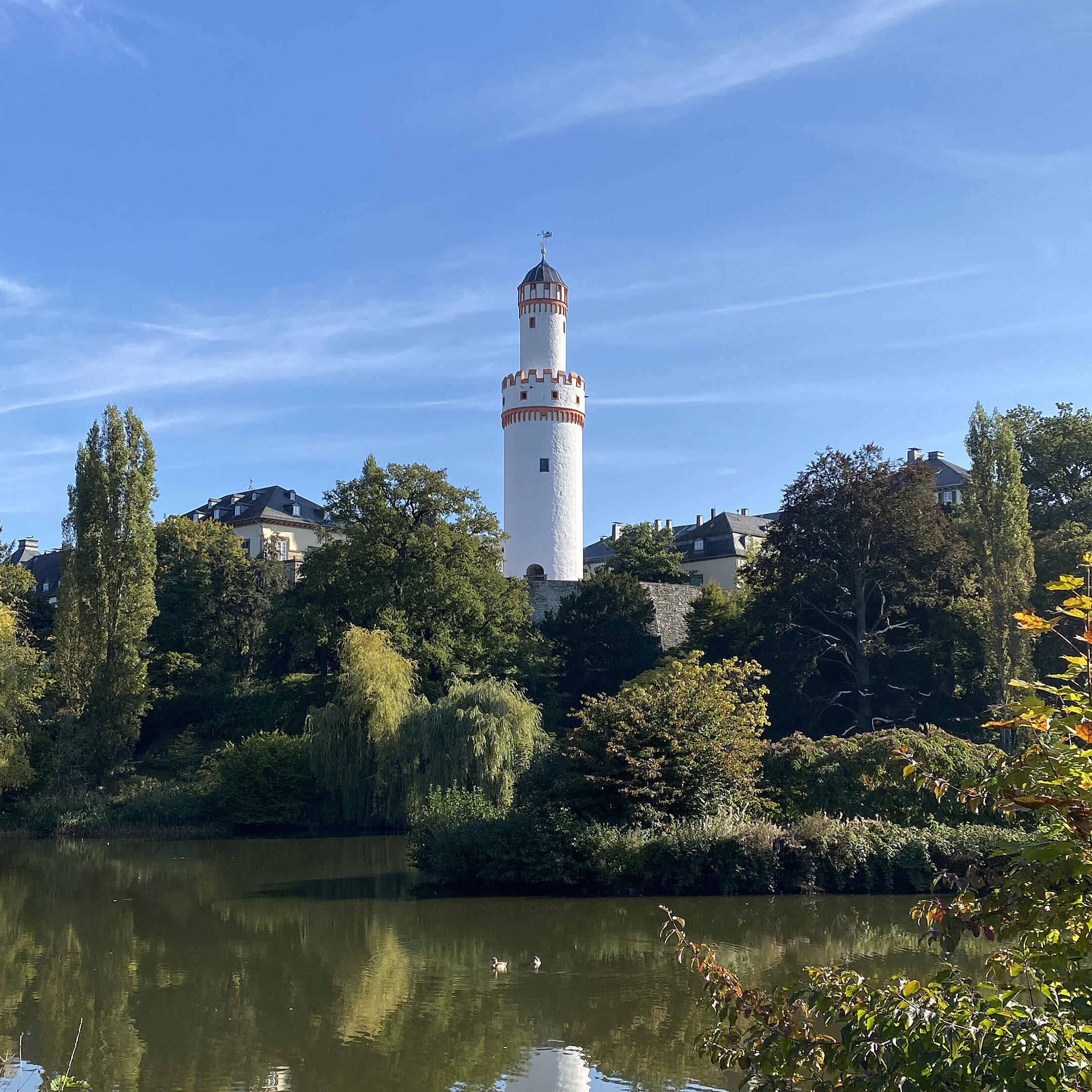 White tower in Bad Homburg with blue sky and surrounded by green nature.