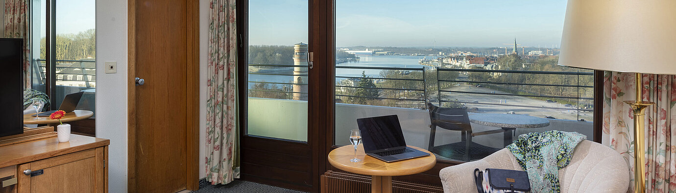 Bright hotel room with balcony, desk and view of the Trave River and Lübeck Bay