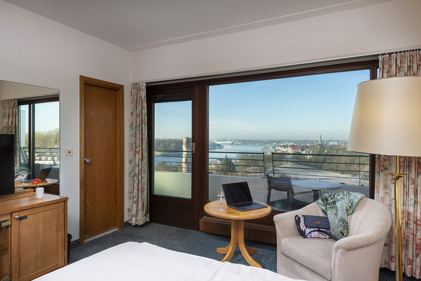 Bright hotel room with balcony, desk and view of the Trave River and Lübeck Bay
