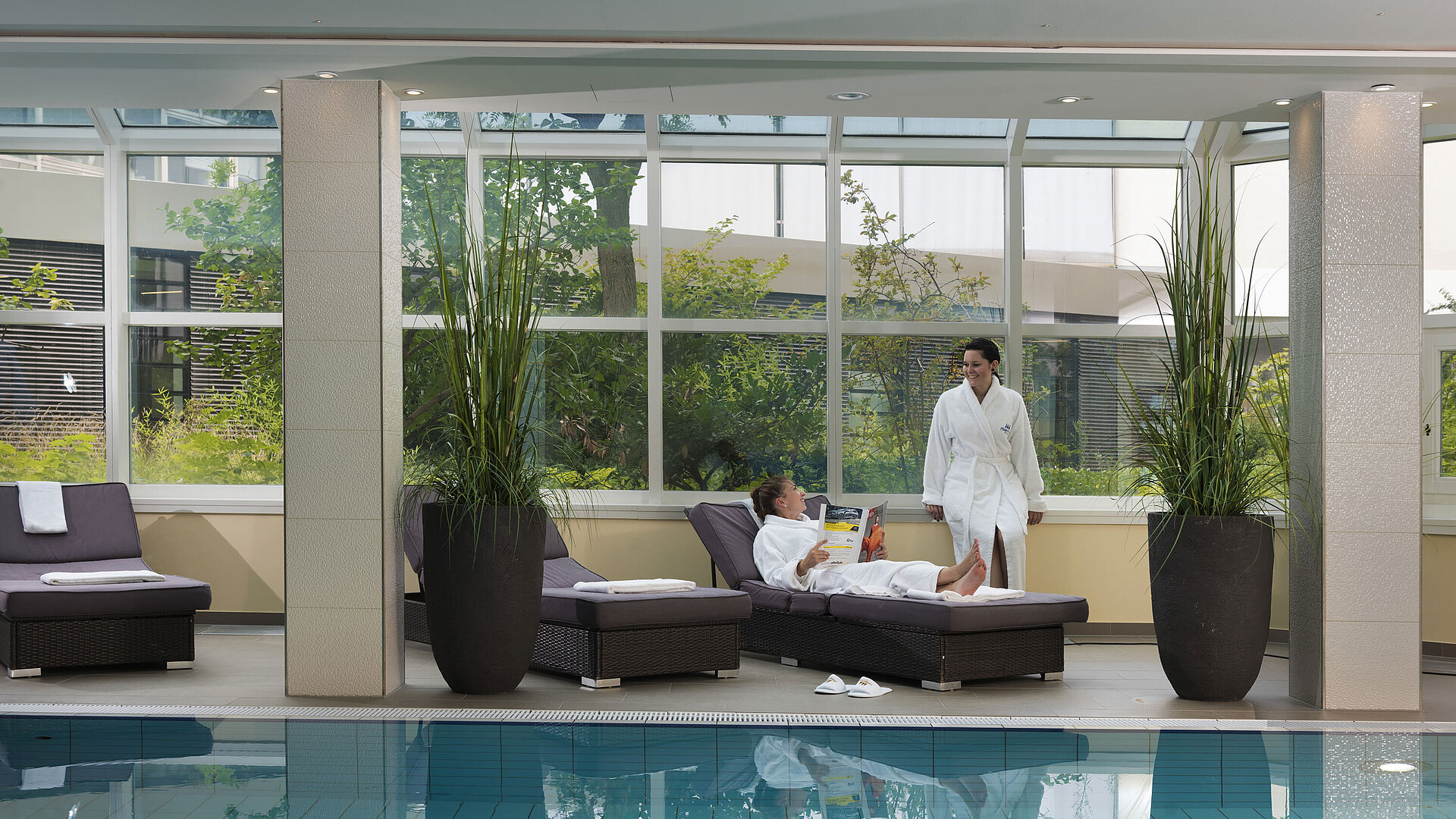Area relax con piscina e lettini al Maritim Hotel Würzburg – ospiti in accappatoio.