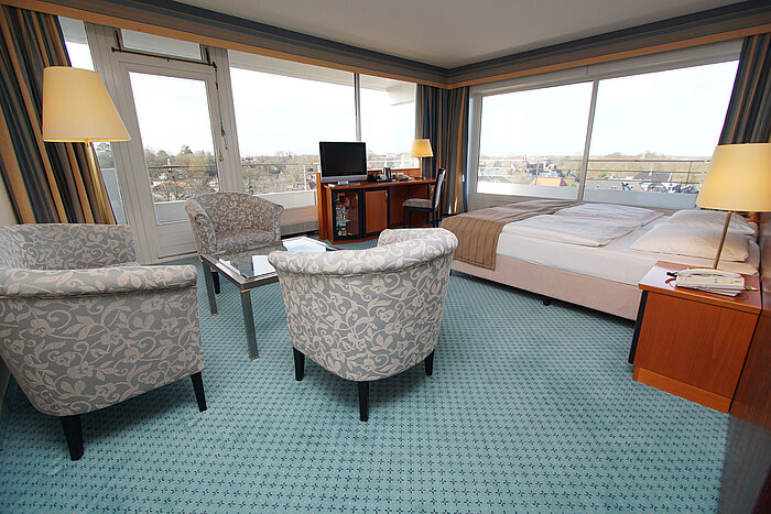 Chambres confortables au Maritim Hotel Kiel, avec coin salon, bureau, lit double et grandes fenêtres avec vue sur la ville.