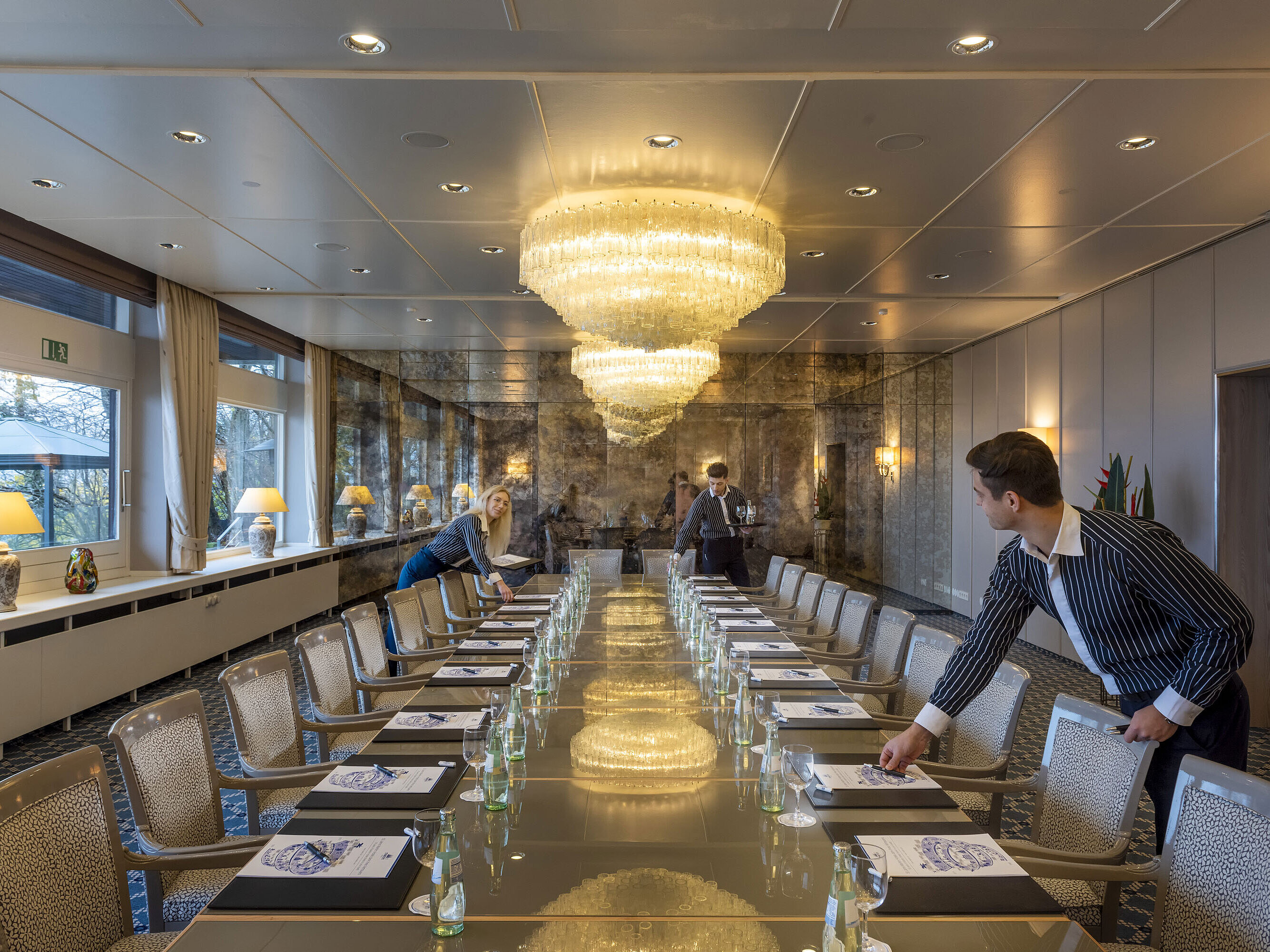 Salón Oslo en el Maritim Hotel Kiel, elegante sala de conferencias con lámparas de araña y una larga hilera de mesas, personal preparando la sala.