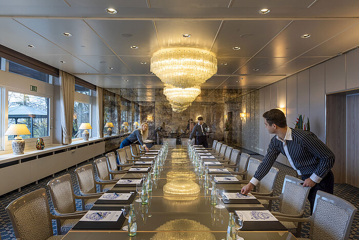Salon Oslo nel Maritim Hotel Kiel, elegante sala conferenze con lampadari e una lunga fila di tavoli, lo staff allestisce la sala.