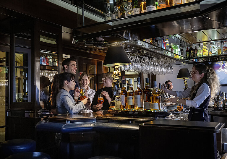 Huéspedes disfrutando de cócteles y buen ambiente en el bar del Hotel Maritim Darmstadt. Personal amable sirviendo bebidas.