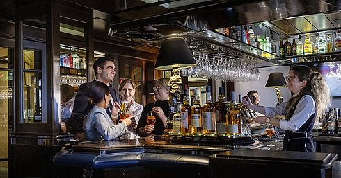 Huéspedes disfrutando de cócteles y buen ambiente en el bar del Hotel Maritim Darmstadt. Personal amable sirviendo bebidas.