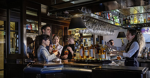 Huéspedes disfrutando de cócteles y buen ambiente en el bar del Hotel Maritim Darmstadt. Personal amable sirviendo bebidas.