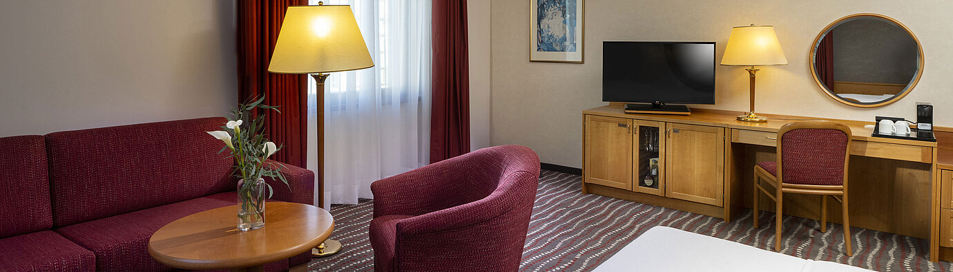 Studio confortable au Maritim Hotel Magdeburg avec coin salon, bureau et télévision moderne.
