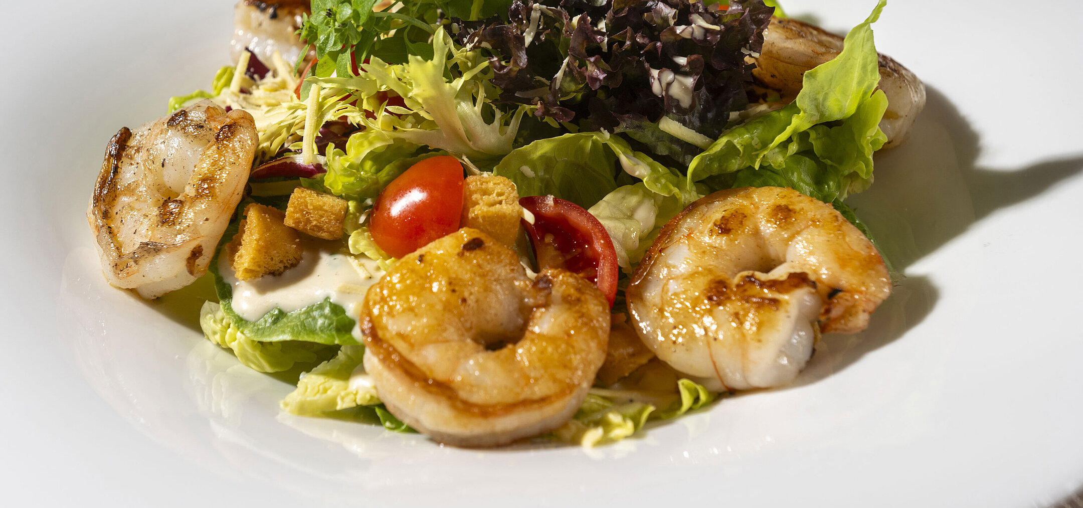 Pan-fried prawns served on fresh leaf salad with cherry tomatoes and Mediterranean accompaniments.