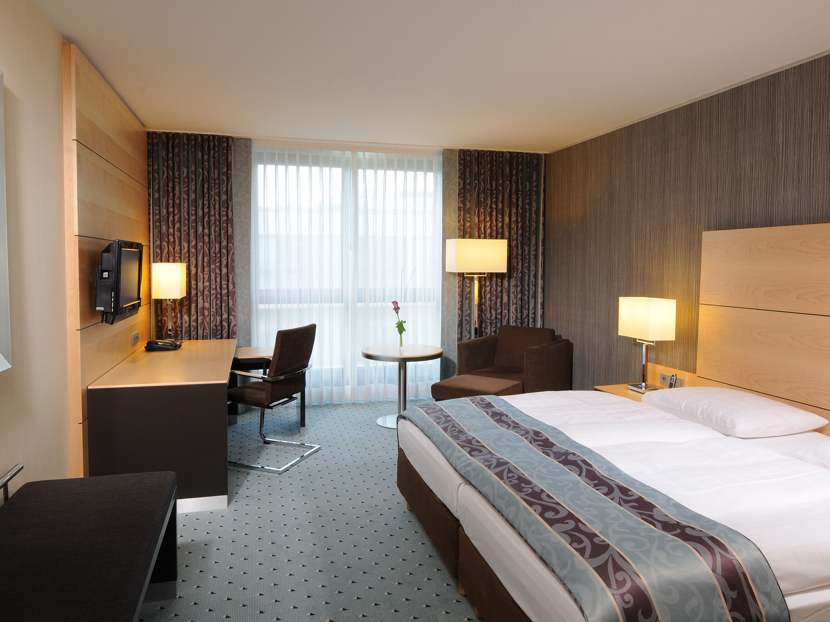 Comfort room at Maritim Hotel Düsseldorf with stylish double bed, cozy seating area, desk, and bright window front.