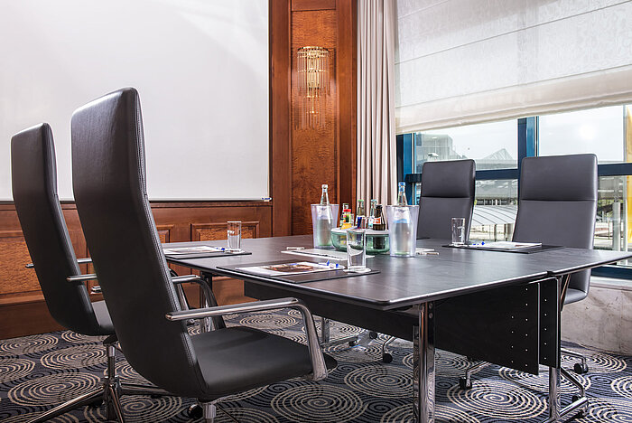 Sala de reuniones moderna con mesa grande, sillas de cuero y luz natural.