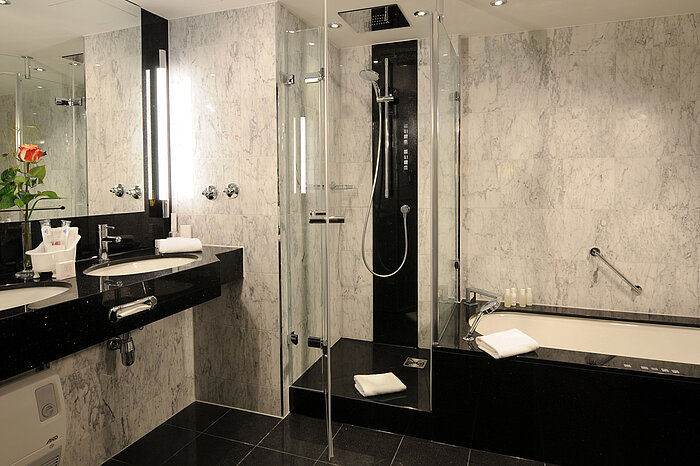 Baño moderno con mármol, ducha, bañera y doble lavabo en Maritim Hotel Múnich