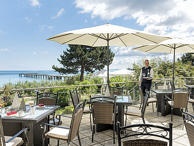 Terrasse de restaurant avec vue sur la mer et parasols au Maritim Seehotel Timmendorfer Strand.