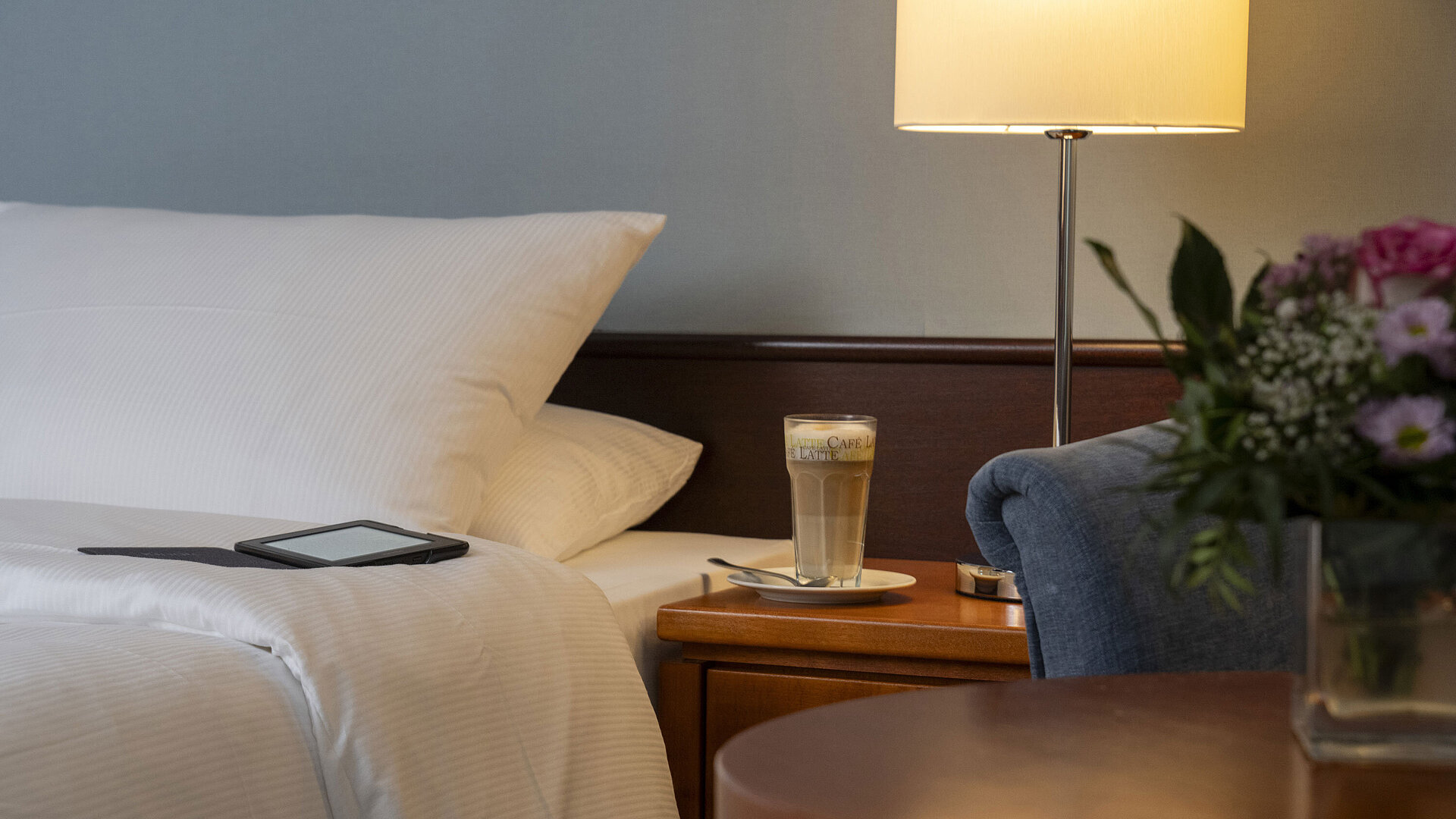 Close-up of a cozy Classic room at Maritim Hotel Darmstadt with a bed, bedside table, latte macchiato, and modern lighting.