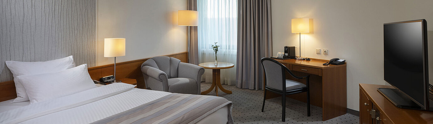 Habitación Superior espaciosa con cama, escritorio, TV y diseño de iluminación cálida en el Maritim Hotel Hannover.