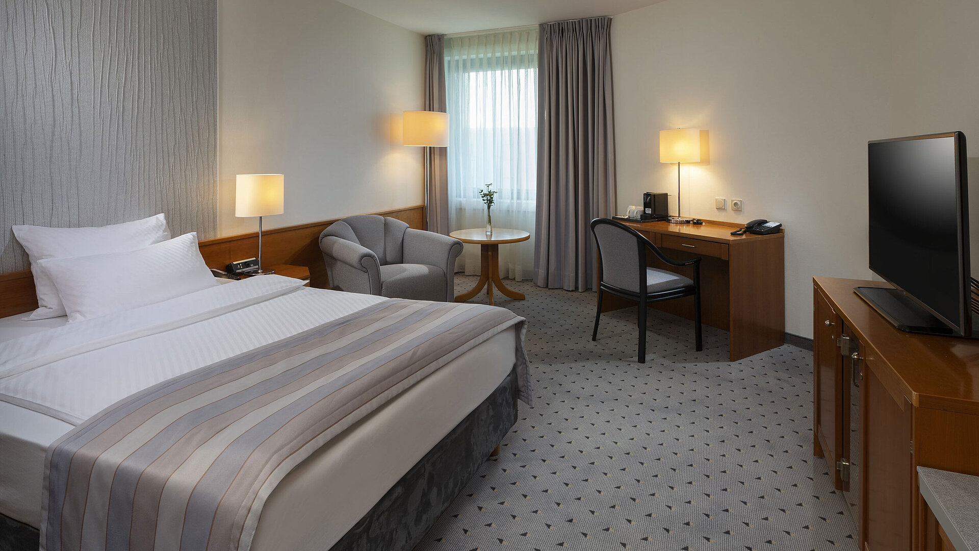 Habitación Superior espaciosa con cama, escritorio, TV y diseño de iluminación cálida en el Maritim Hotel Hannover.