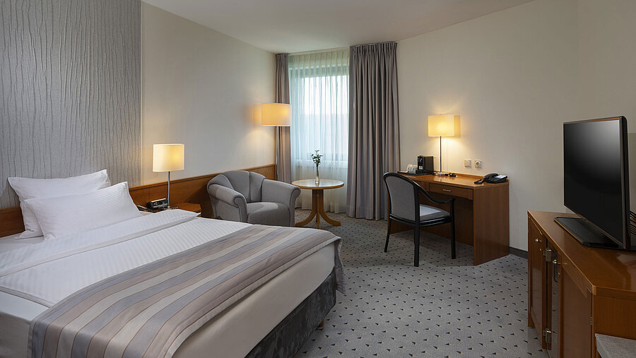 Habitación Superior espaciosa con cama, escritorio, TV y diseño de iluminación cálida en el Maritim Hotel Hannover.
