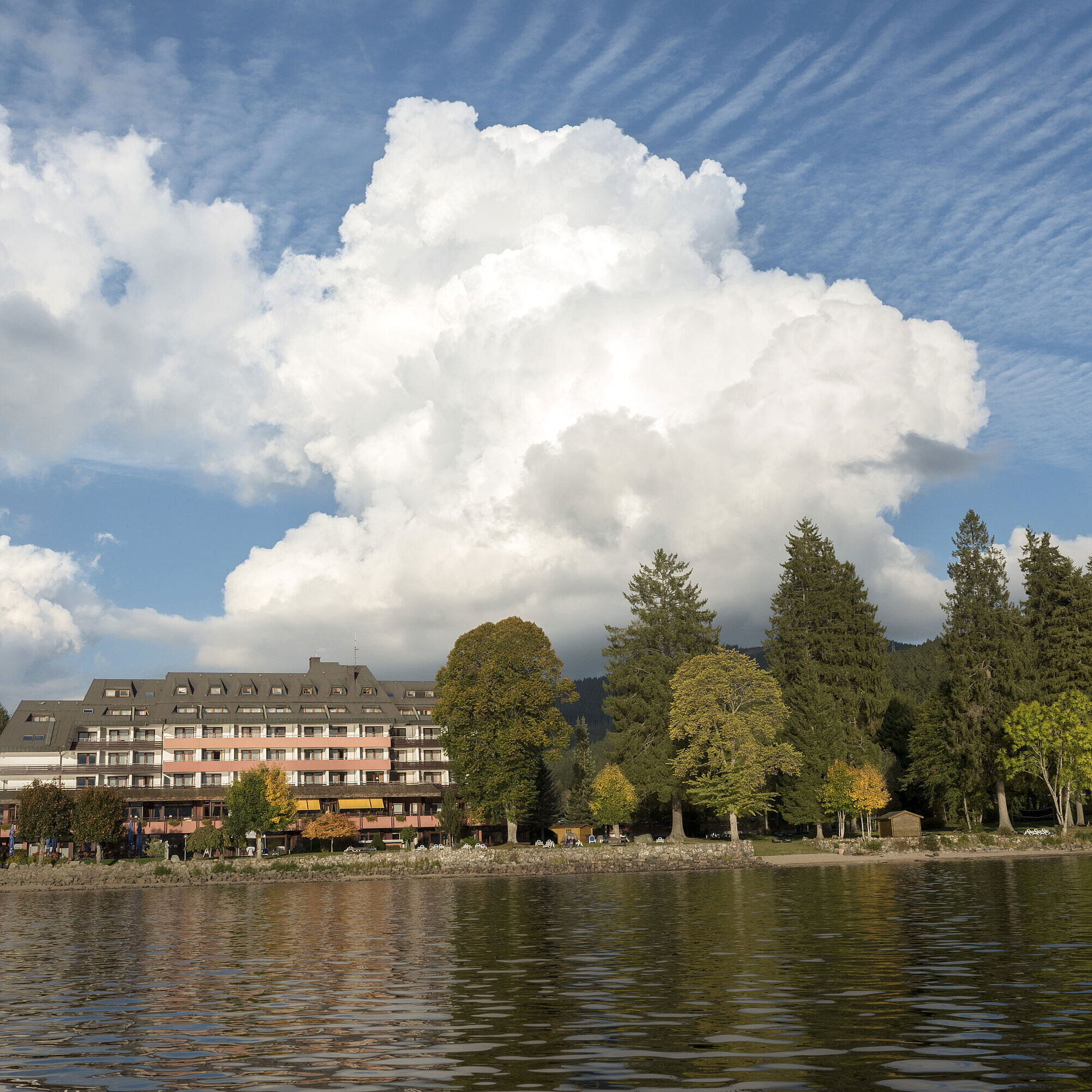 Vista exterior del Maritim Hotel Titisee con árboles y lago bajo el cielo azul