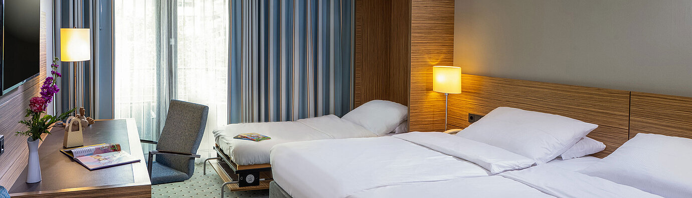 Habitación Familiar Comfort en el Maritim Hotel Darmstadt con cama doble, cama supletoria y zona de trabajo moderna