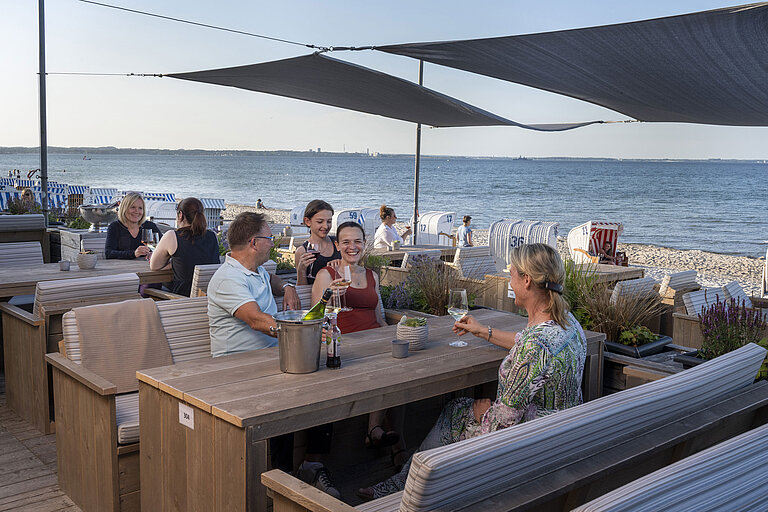 Groupe de clients au bar de plage du Maritim Timmendorfer Strand dégustant des boissons avec vue sur la mer et chaises.