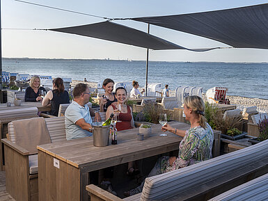 Group of guests at the beach bar of Maritim Seehotel Timmendorfer Strand enjoying drinks with sea view and beach chairs.