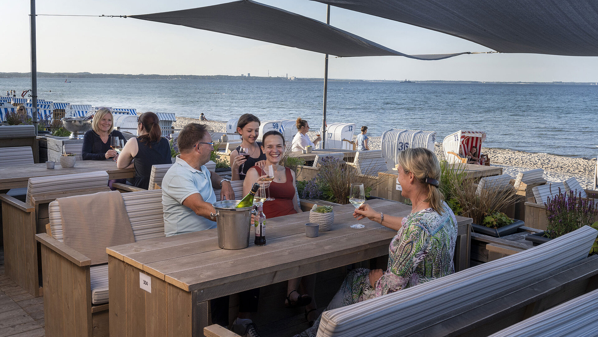 Gruppo di ospiti al bar sulla spiaggia del Maritim Seehotel Timmendorfer Strand che beve con vista mare e sdraio.