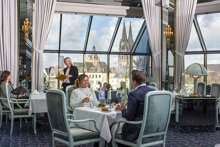 Restaurante Bellevue en el Hotel Maritim Colonia con huéspedes cenando y vista a la catedral de Colonia por grandes ventanas