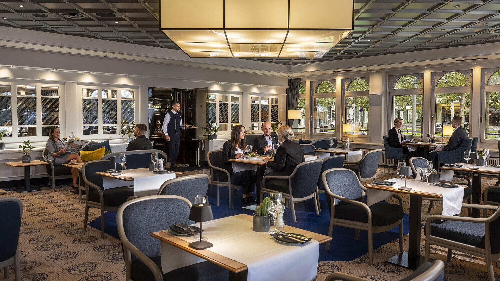 Elegant restaurant at Maritim Hotel Darmstadt with guests dining and relaxing. Modern decor and large windows with a view.