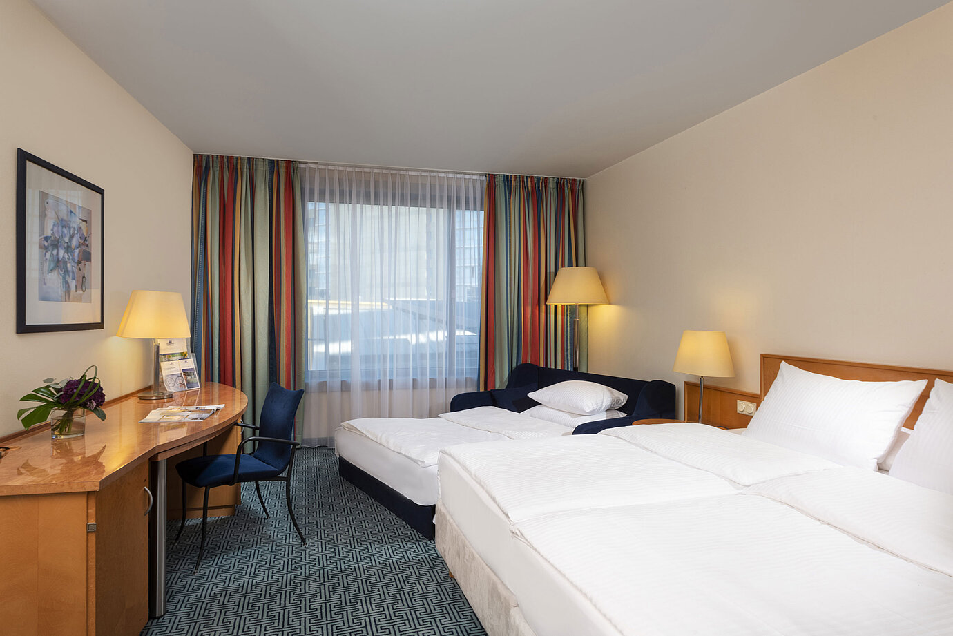 Chambre familiale Classic du Maritim Hotel Frankfurt avec lit double, canapé-lit, bureau et rideaux colorés.