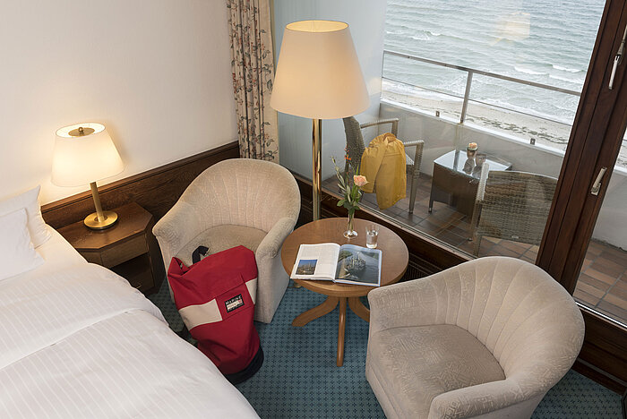 Seating area with two armchairs, table, and balcony view of the sea at Maritim Seehotel Timmendorfer Strand.