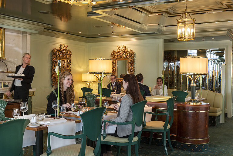 Los huéspedes disfrutan de su comida en el elegante restaurante «La Galerie», rodeado de elegantes espejos y lámparas.