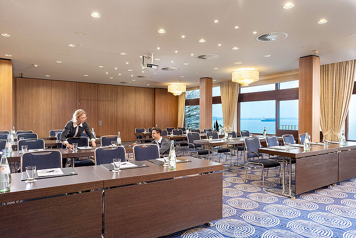 Saal Kiel nel Maritim Hotel Kiel, ampia sala conferenze con vista sul mare, personale cordiale che allestisce i tavoli.