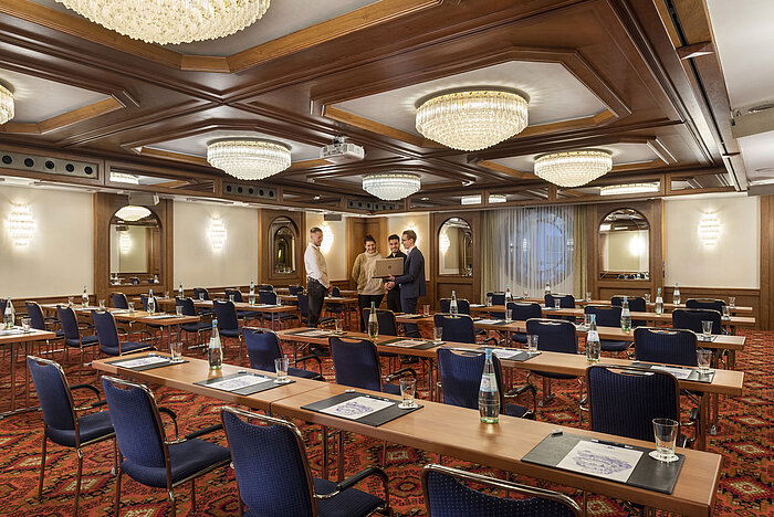 El salón Colonia con elegantes candelabros y filas de asientos en un ambiente clásico de sala de conferencias.