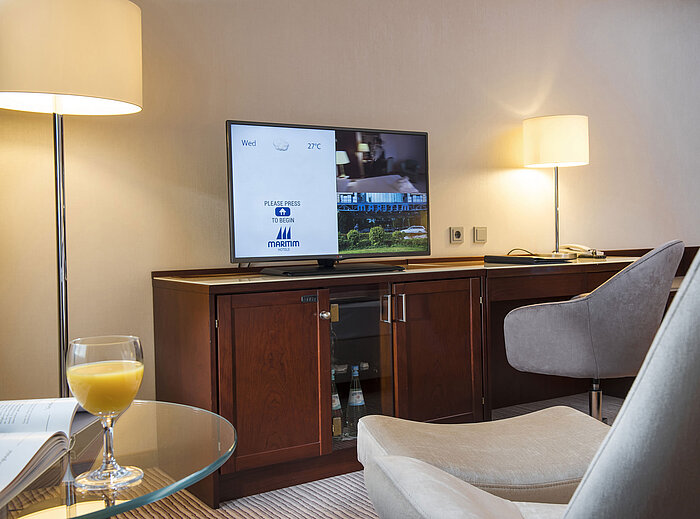 Detalle de una habitación en el Maritim Hotel Bonn con TV, escritorio y vaso de zumo de naranja en la mesa.