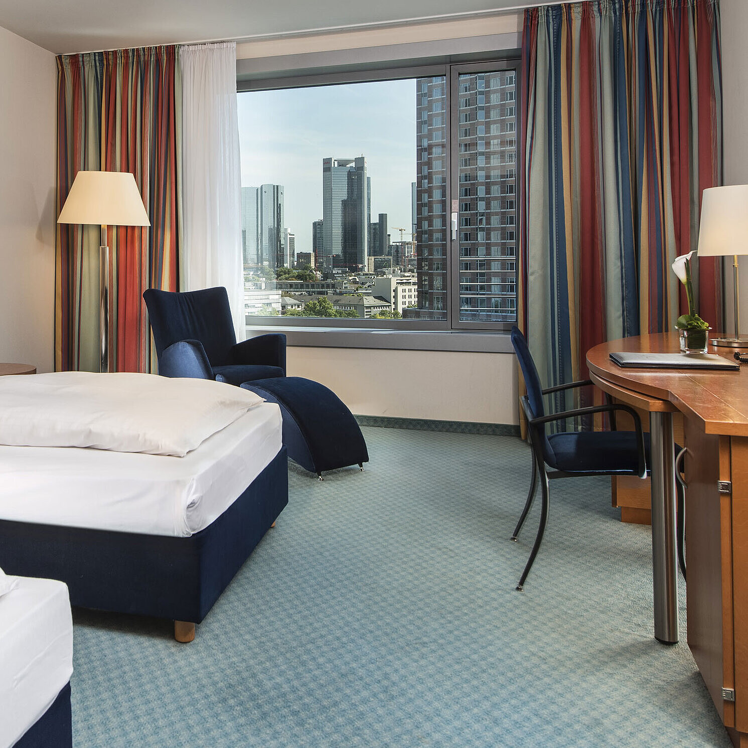 Camera comfort al Maritim Hotel Frankfurt con due letti singoli, scrivania, area salotto e vista sulla skyline.
