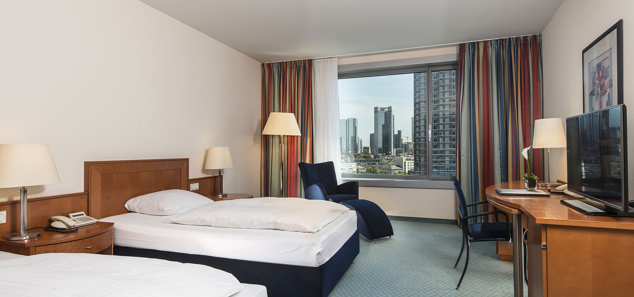 Camera comfort al Maritim Hotel Frankfurt con due letti singoli, scrivania, area salotto e vista sulla skyline.