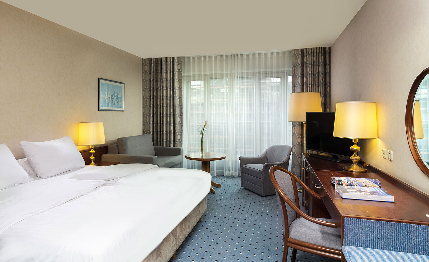 Bright family room at Maritim Hotel Cologne with double bed, desk, TV, armchairs, and large windows with curtains.