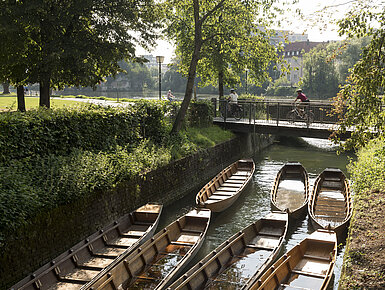 Wooden boats in a side channel of the Danube in Ulm, surrounded by green trees.