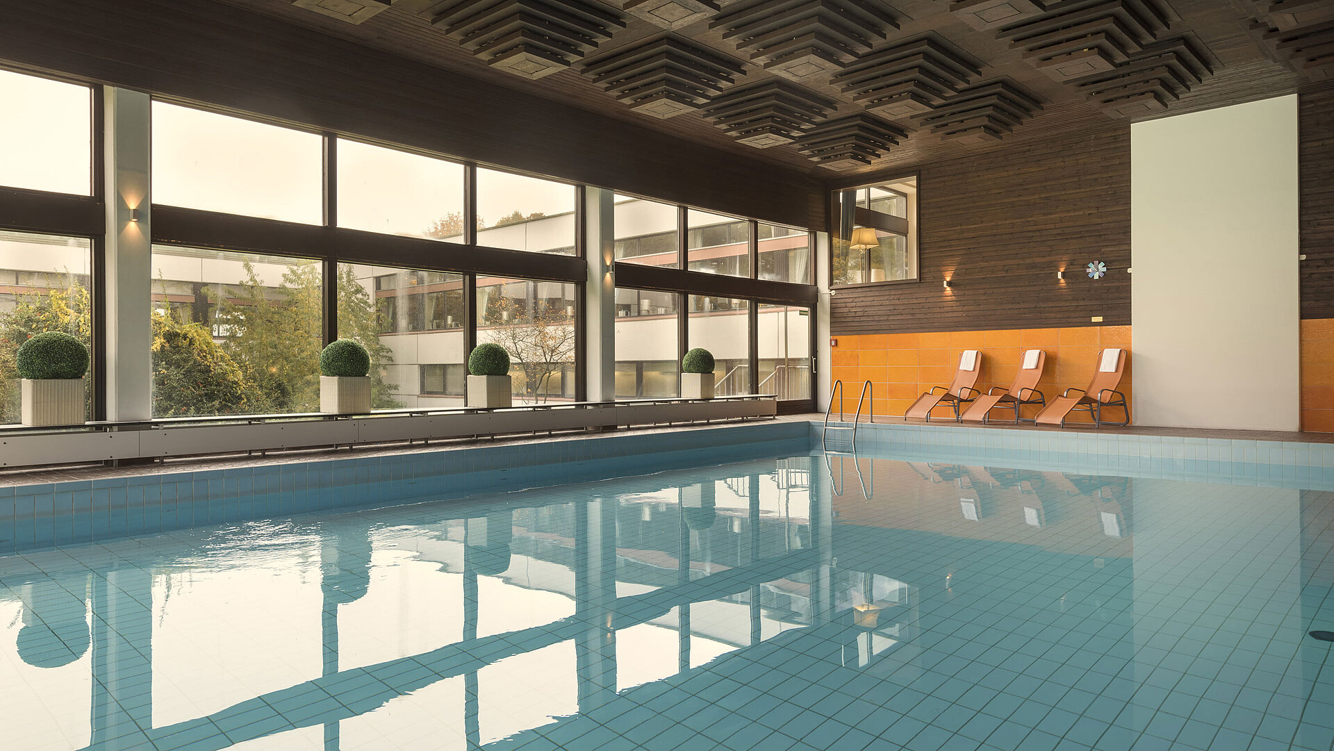 The picture shows the indoor pool of the Maritim Hotel Kiel, surrounded by large windows, with sun loungers for relaxation.